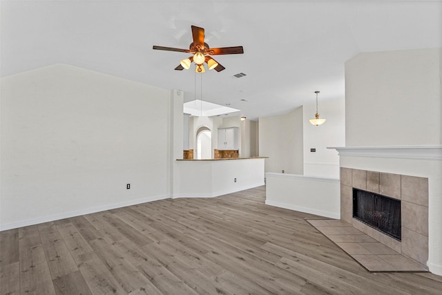 unfurnished living room featuring a tiled fireplace, light hardwood / wood-style floors, ceiling fan, and lofted ceiling