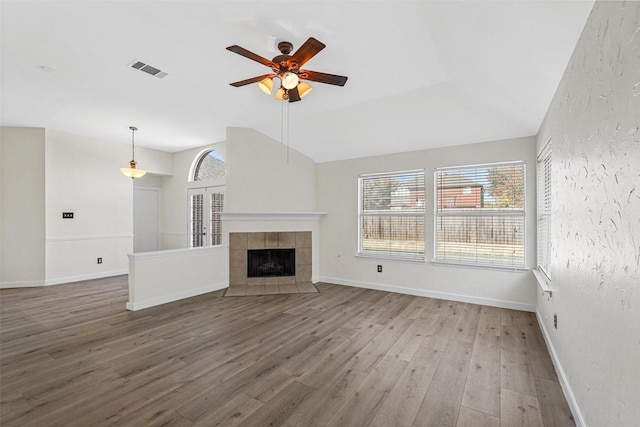 unfurnished living room with ceiling fan, a healthy amount of sunlight, a tiled fireplace, and wood-type flooring