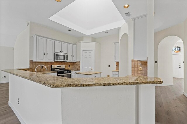 kitchen with appliances with stainless steel finishes, white cabinets, light stone counters, and kitchen peninsula