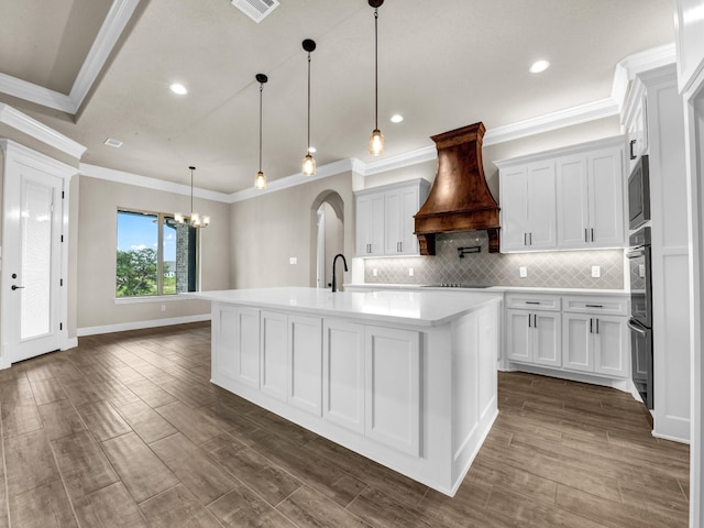 kitchen with dark hardwood / wood-style flooring, decorative light fixtures, a kitchen island with sink, white cabinets, and custom range hood