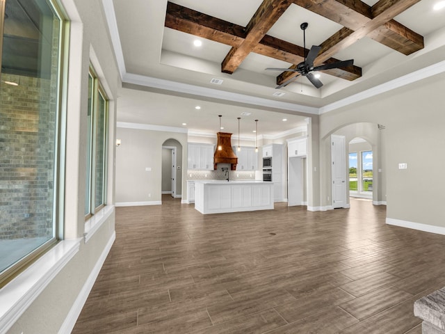 unfurnished living room with beam ceiling, ceiling fan, coffered ceiling, dark hardwood / wood-style floors, and ornamental molding