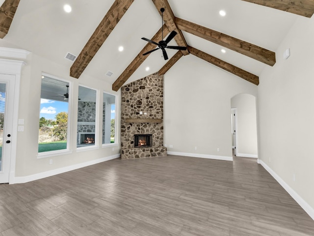 unfurnished living room with beamed ceiling, a stone fireplace, wood-type flooring, and high vaulted ceiling