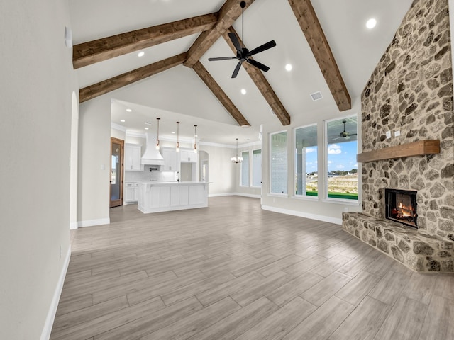 unfurnished living room featuring light hardwood / wood-style flooring, high vaulted ceiling, beamed ceiling, a fireplace, and ceiling fan with notable chandelier