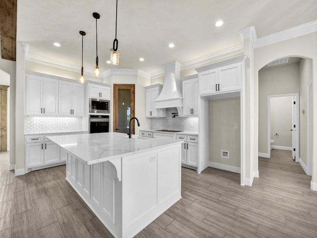 kitchen with white cabinetry, custom range hood, an island with sink, and appliances with stainless steel finishes