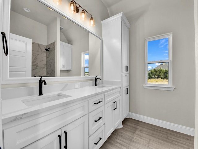 bathroom with hardwood / wood-style floors, vanity, a tile shower, and lofted ceiling