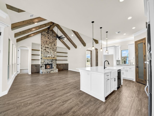 kitchen with dark wood-type flooring, lofted ceiling with beams, a fireplace, white cabinets, and a center island with sink