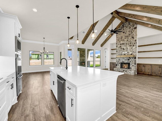 kitchen with hanging light fixtures, beamed ceiling, an island with sink, a fireplace, and white cabinets