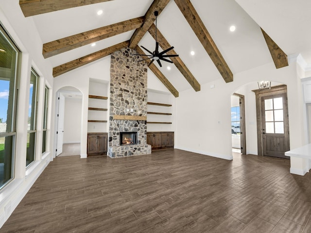 unfurnished living room featuring dark hardwood / wood-style flooring, high vaulted ceiling, beamed ceiling, a fireplace, and ceiling fan with notable chandelier