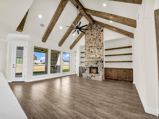 unfurnished living room featuring dark wood-type flooring, high vaulted ceiling, a stone fireplace, ceiling fan, and beam ceiling