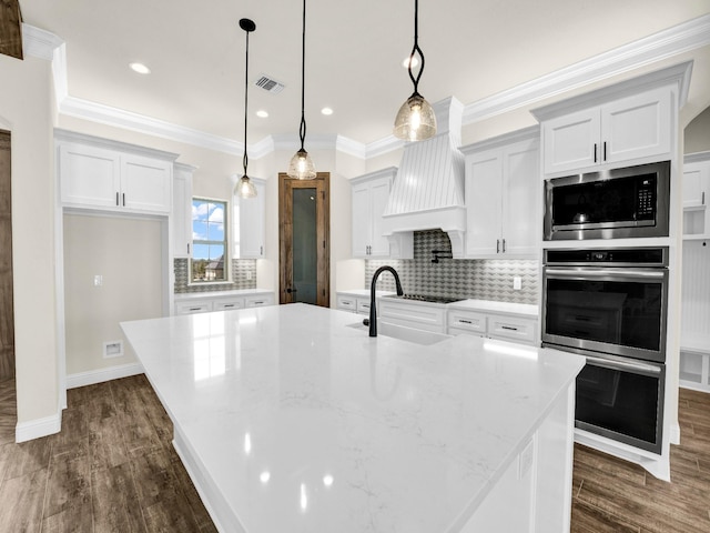 kitchen featuring a center island with sink, decorative light fixtures, and light stone countertops