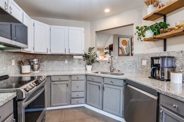 kitchen with light stone countertops, white cabinetry, sink, stainless steel appliances, and dark tile patterned flooring