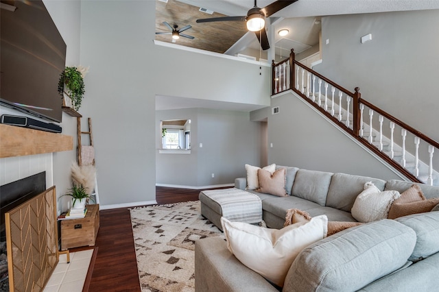 living room with ceiling fan, a fireplace, hardwood / wood-style floors, and a towering ceiling