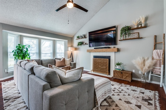 living room with vaulted ceiling, hardwood / wood-style flooring, ceiling fan, a textured ceiling, and a tiled fireplace