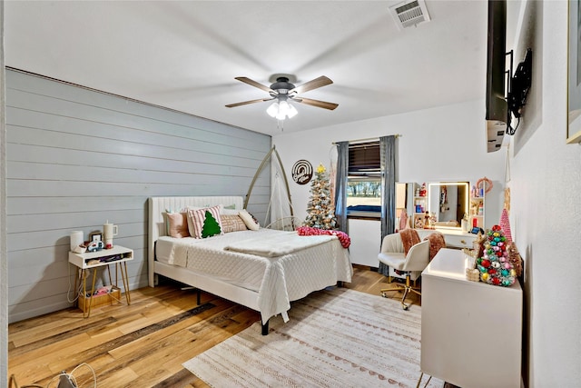 bedroom featuring hardwood / wood-style flooring, ceiling fan, and wooden walls