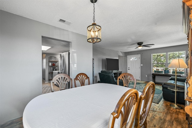 dining room with a textured ceiling, ceiling fan with notable chandelier, and dark hardwood / wood-style floors