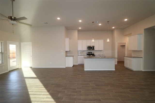 kitchen featuring white cabinets, a center island with sink, ceiling fan, appliances with stainless steel finishes, and tasteful backsplash