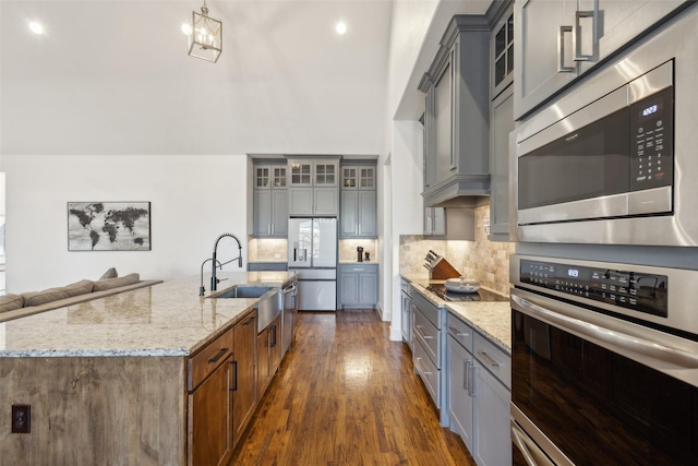 kitchen with light stone countertops, sink, stainless steel appliances, dark hardwood / wood-style flooring, and a center island with sink