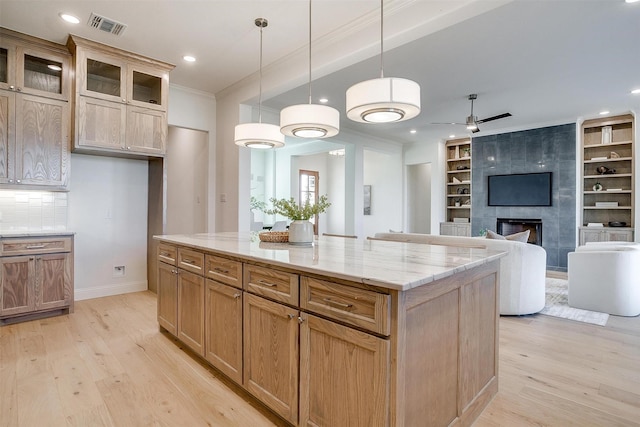 kitchen featuring a center island, built in shelves, light wood-type flooring, decorative light fixtures, and light stone counters