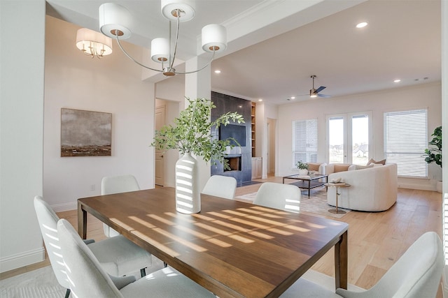 dining area with a large fireplace, light hardwood / wood-style floors, ceiling fan with notable chandelier, and ornamental molding