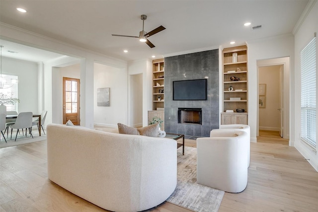 living room featuring built in shelves, ceiling fan, a fireplace, and light hardwood / wood-style floors