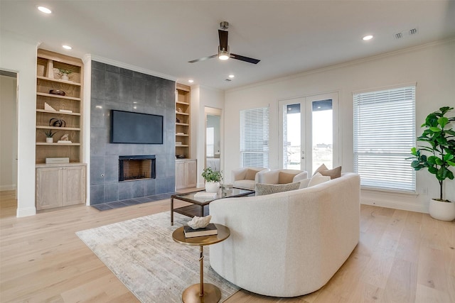 living room featuring built in shelves, light hardwood / wood-style floors, ceiling fan, and a tiled fireplace