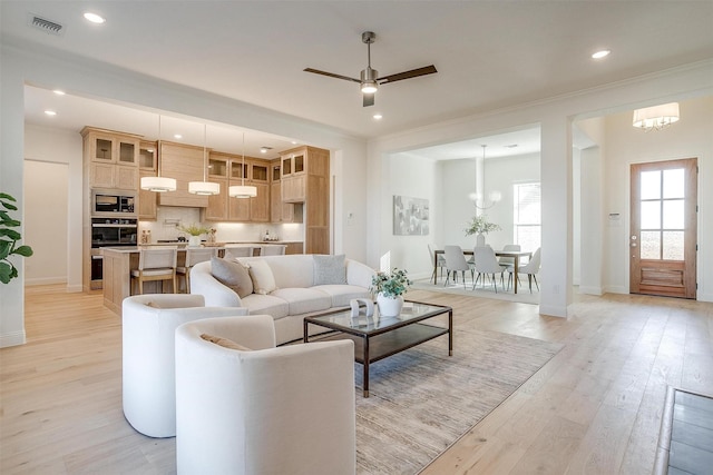 living room featuring ceiling fan with notable chandelier, light hardwood / wood-style floors, and ornamental molding