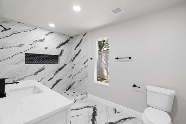 bathroom with tiled shower, vanity, and toilet