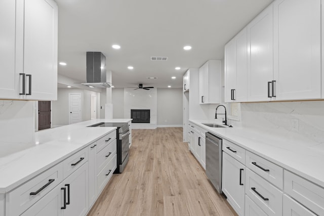 kitchen with white cabinetry, sink, stainless steel appliances, wall chimney range hood, and a premium fireplace