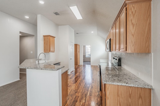 kitchen with kitchen peninsula, appliances with stainless steel finishes, a textured ceiling, vaulted ceiling, and dark wood-type flooring