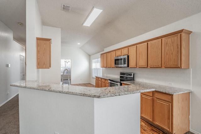 kitchen with light stone counters, kitchen peninsula, wood-type flooring, lofted ceiling, and appliances with stainless steel finishes