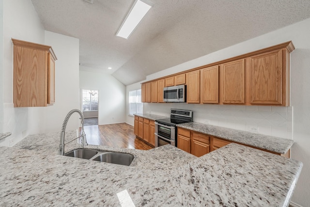 kitchen with kitchen peninsula, light wood-type flooring, stainless steel appliances, vaulted ceiling, and sink