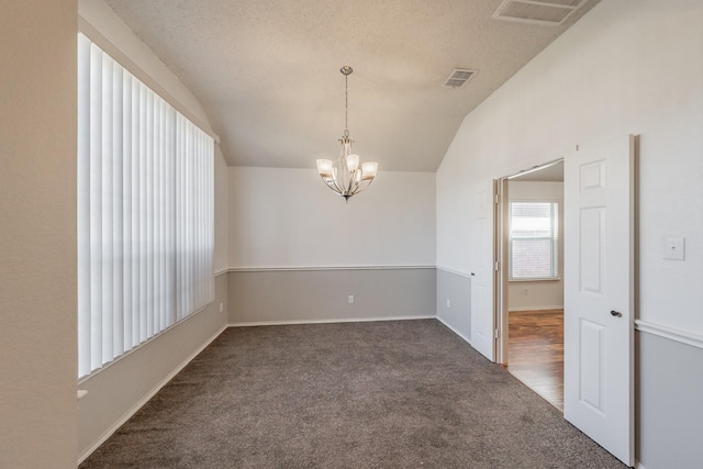 carpeted empty room featuring a textured ceiling, vaulted ceiling, and a notable chandelier