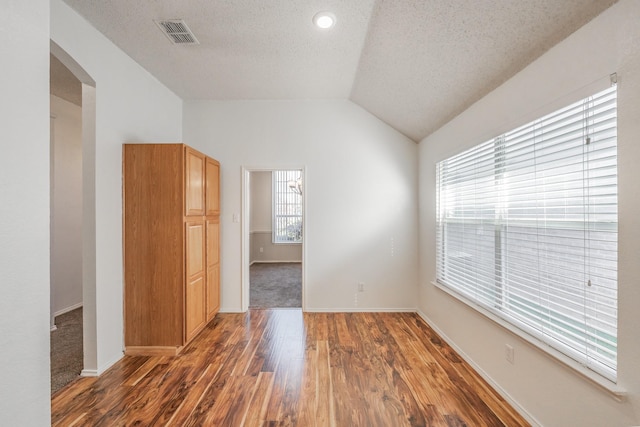 spare room featuring dark hardwood / wood-style floors, lofted ceiling, and a textured ceiling