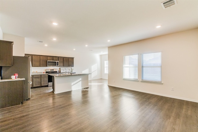 kitchen featuring dark wood-type flooring, sink, light stone countertops, an island with sink, and appliances with stainless steel finishes