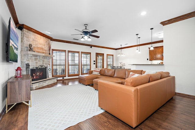 living room featuring ceiling fan, ornamental molding, dark hardwood / wood-style flooring, and a stone fireplace