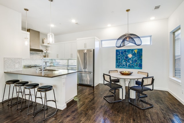 kitchen with kitchen peninsula, high end refrigerator, dark wood-type flooring, pendant lighting, and white cabinetry