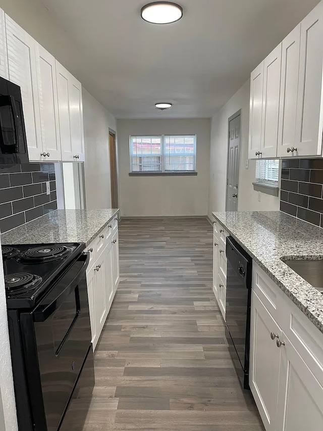 kitchen with light stone countertops, white cabinets, black appliances, and hardwood / wood-style flooring