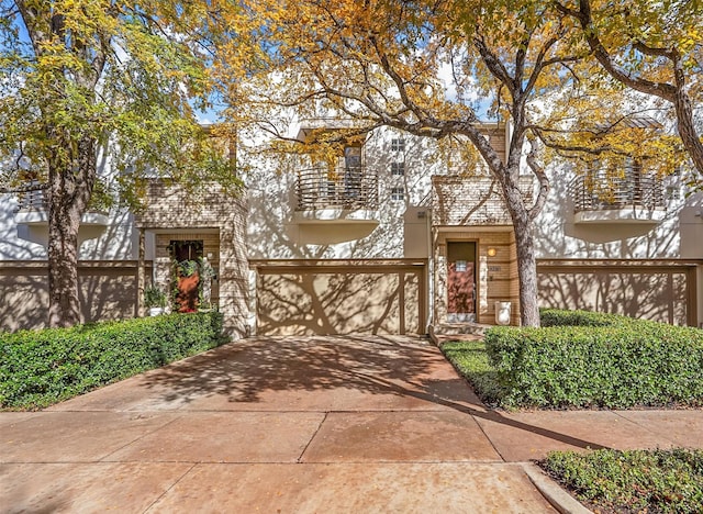 mid-century modern home with an attached garage, a balcony, brick siding, concrete driveway, and stucco siding