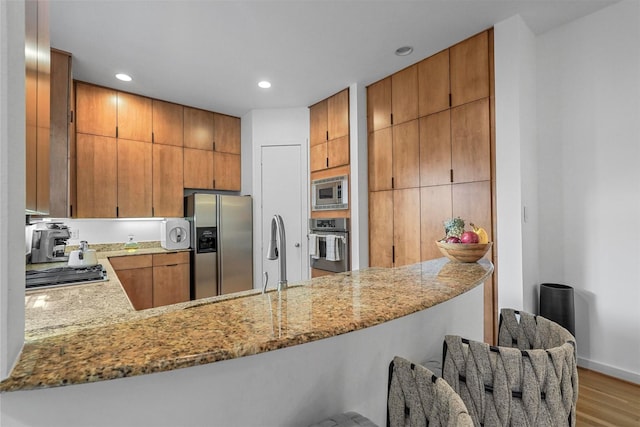 kitchen with light stone countertops, kitchen peninsula, appliances with stainless steel finishes, and light hardwood / wood-style flooring