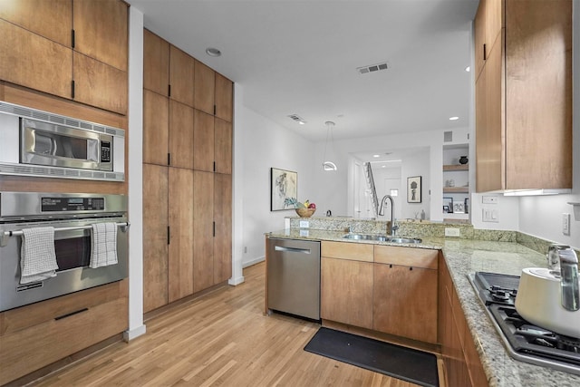 kitchen featuring sink, kitchen peninsula, light hardwood / wood-style floors, decorative light fixtures, and appliances with stainless steel finishes