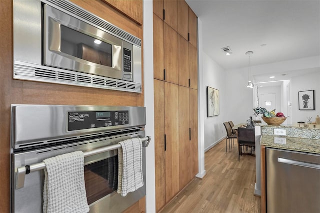 kitchen with stainless steel appliances, hanging light fixtures, and light hardwood / wood-style floors