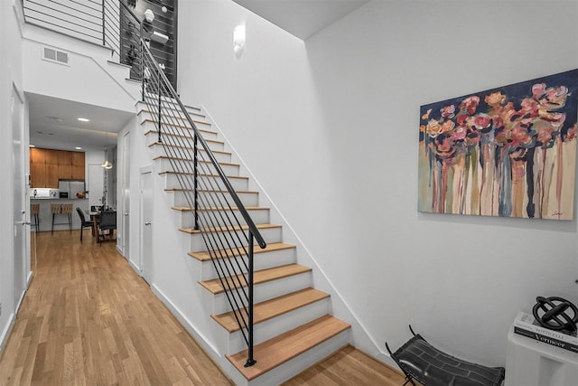 stairway with hardwood / wood-style floors and a towering ceiling