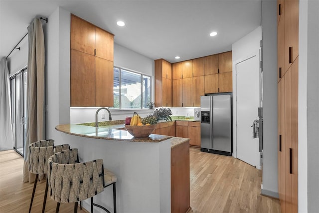 kitchen with sink, stainless steel fridge with ice dispenser, light wood-type flooring, kitchen peninsula, and a breakfast bar area