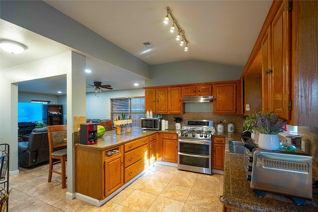 kitchen featuring stone counters, vaulted ceiling, appliances with stainless steel finishes, a kitchen breakfast bar, and ceiling fan