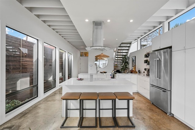 kitchen with island range hood, white cabinets, decorative light fixtures, high end fridge, and a kitchen bar