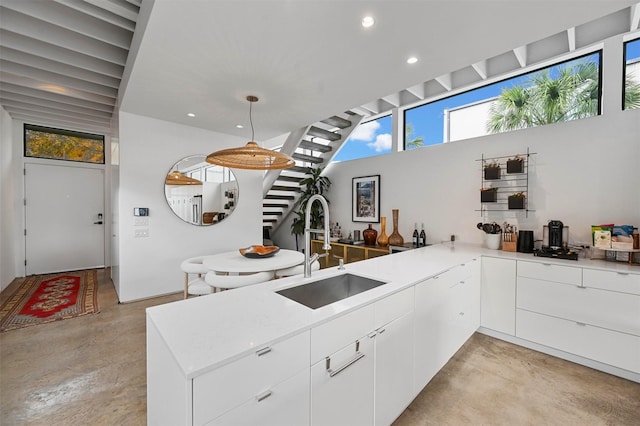 kitchen featuring kitchen peninsula, pendant lighting, white cabinetry, and sink