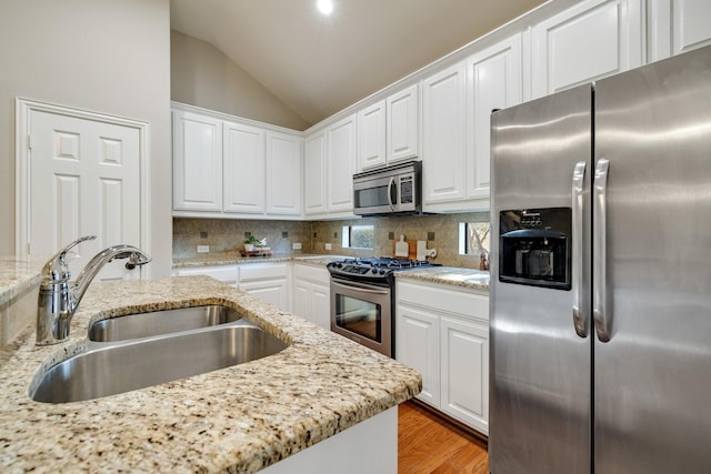 kitchen featuring stainless steel appliances, lofted ceiling, decorative backsplash, white cabinets, and a sink