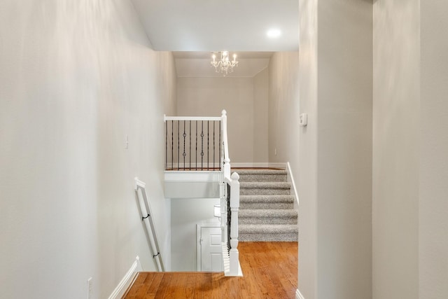 staircase featuring an inviting chandelier, baseboards, and wood finished floors