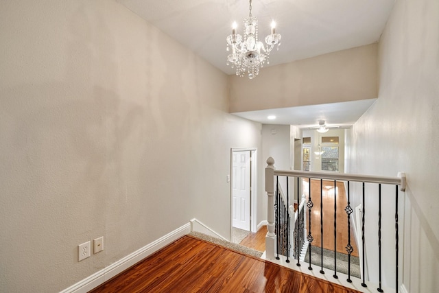 hallway featuring a notable chandelier, wood finished floors, an upstairs landing, and baseboards