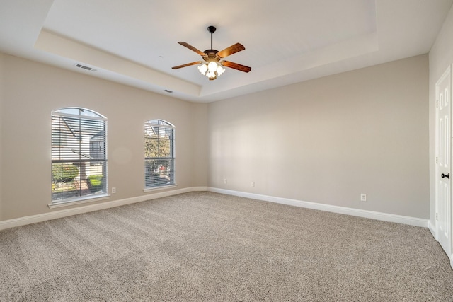 carpeted empty room featuring a raised ceiling, visible vents, and baseboards